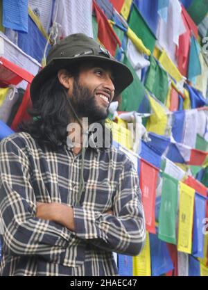A happy young guy looking sideways posing with crossing his arms, standing against Buddhist prayer flags Stock Photo