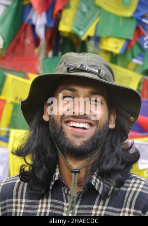 Closeup of a happy bearded and long haired young man looking at camera, posing against tibetan prayer flags Stock Photo