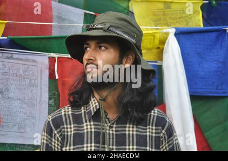 A bearded and long haired male tourist looking sideways while standing against tibetan prayer flags Stock Photo