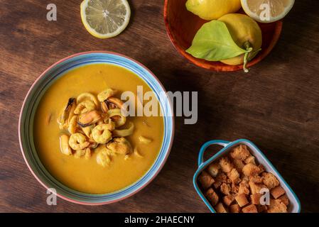 Seafood soup, based on prawns, mussels, clams, hake and squid, served with fried bread and lemons, on a dark wooden table. Stock Photo