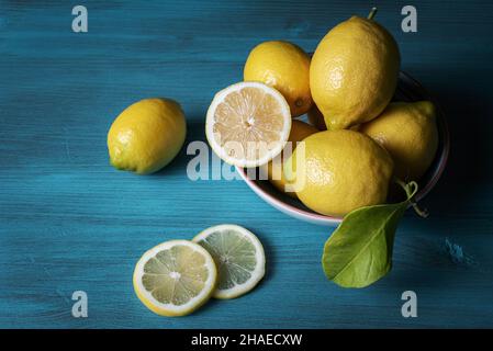 Lemons in a bowl and two loose slices, all on a light blue wooden table. Stock Photo