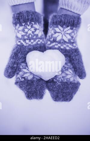 Color of the Year 2022 Very Peri. A girl in knitted red mittens holding a heart made of snow on her palms. Valentine's day concept. Declaration of Stock Photo