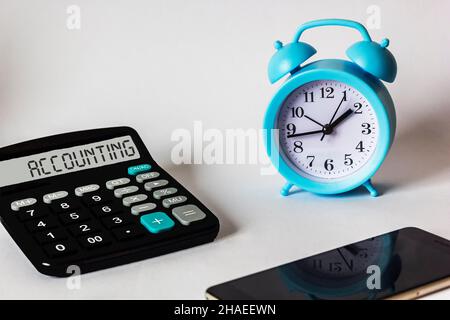 Accounting, the word is written on the display of a calculator that lies on a white background with an alarm clock and a mobile phone Stock Photo