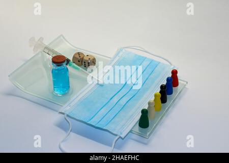 Medical syringe, vaccine vial and surgical face mask on glass tray beside game dice. Concept of number of Covid-19 vaccine doses and booster injection Stock Photo