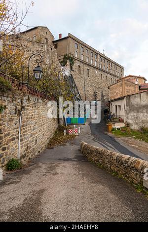 A narrow lane runs along the old town wall to one of the houses in the Quartier Saint-Ennemond, the historic centre of Saint-Chamond, Loire department, France. The town has sold dilapidated houses here, along with the land, for a symbolic one euro, on condition that they are fully restored; the quarter on the castle hill is today mostly inhabited by guest-worker families. Scaffolding covered with a green tarpaulin on one of the buildings shows such a restoration under way. Stock Photo
