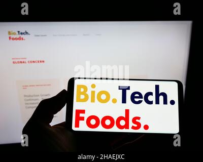 Person holding cellphone with logo of Spanish cultured meat company BioTech Foods on screen in front of business webpage. Focus on phone display. Stock Photo