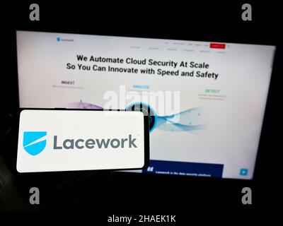 Person holding mobile phone with logo of US cloud security company Lacework Inc. on screen in front of business web page. Focus on phone display. Stock Photo