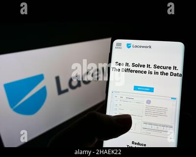 Person holding smartphone with webpage of US cloud security company Lacework Inc. on screen in front of logo. Focus on center of phone display. Stock Photo