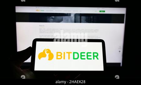 Person holding cellphone with logo of Singaporean blockchain mining company Bitdeer Group on screen in front of webpage. Focus on phone display. Stock Photo