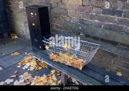 Shopping basket full of Autumn leaves on a bench on 23rd November 2021 in London, United Kingdom. Stock Photo