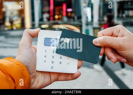 Crop anonymous female customer with credit card making contactless purchase on POS terminal in store in city Stock Photo