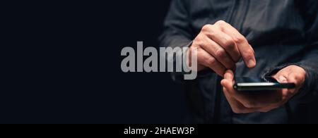 Panoramic closeup of male hands using smartphone for text message communication, copy space included in this low key image with selective focus Stock Photo
