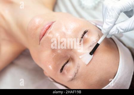 Close-up beautician doctor hand making anti-age procedure apply peeling acid young attractive female client at beauty clinic. Cosmetologist specialist Stock Photo