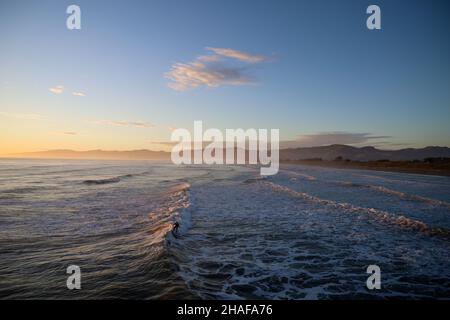 Surfer riding wave at sunrise Stock Photo