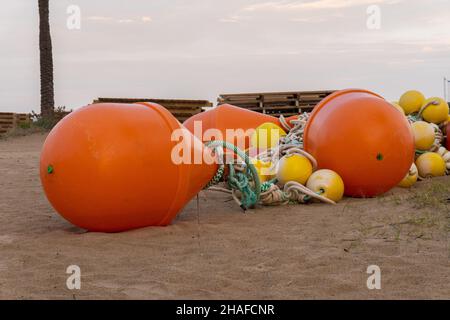 A close-up shot of buoys of different sizes and colors thrown in the sand on a beach Stock Photo