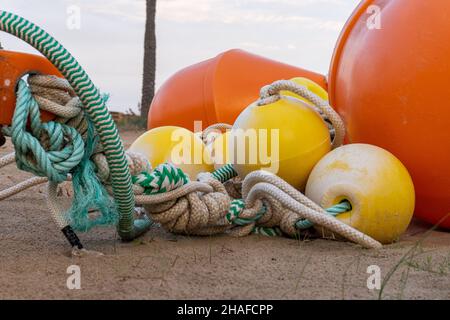 A close-up shot of buoys of different sizes and colors thrown in the sand on a beach Stock Photo