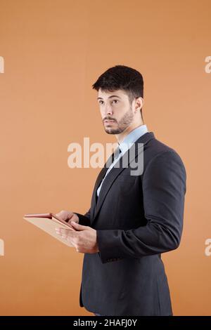 Portrait of surprised young entrepreneur holding tablet computer and looking away, isolated on orange Stock Photo