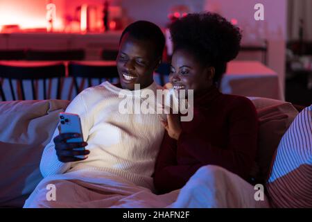 Happy african man and woman relax on sofa with smartphone, talk with family via video chat Stock Photo