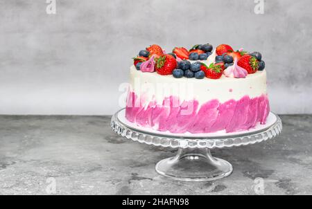 Delicate cake garnished with fresh strawberries blueberries on a gray plain background. Festive dessert Stock Photo
