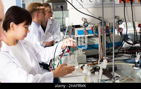Multiracial team of young scientists performing experiments on lab equipment in modern university research laboratory Stock Photo