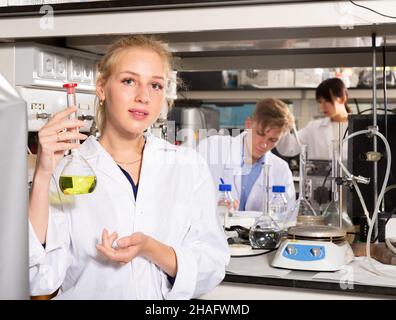 Attractive female student performing experiments in university laboratory, examining chemical substances in glass lab flask Stock Photo