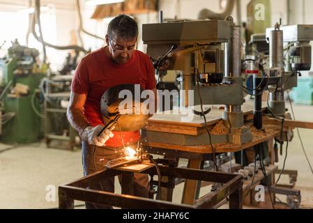 Person in red T-shirt welding in a manufacturing plant Stock Photo