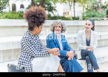 three female workers talking business while sitting in the street Stock Photo