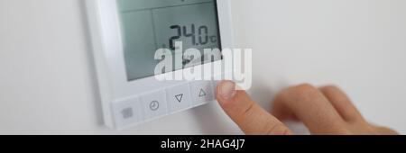 Person regulates air temperature in room through remote control on wall Stock Photo
