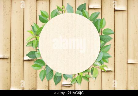 Green leaves and round paper card on bamboo mat texture. Horizontal banner with eco paper texture. Bamboo planks, recycled carton material label and g Stock Photo