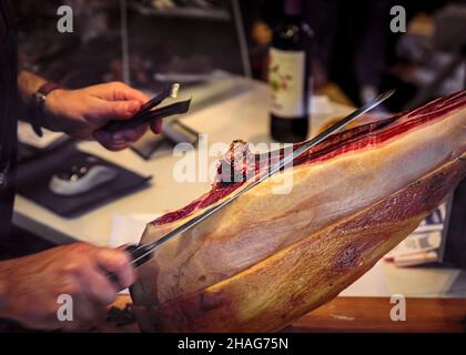 Whole bone-in leg of Spanish serrano iberico ham being carved at a local butcher shop in a restaurant, San Sebastian Donostia, Basque Country, Spain Stock Photo