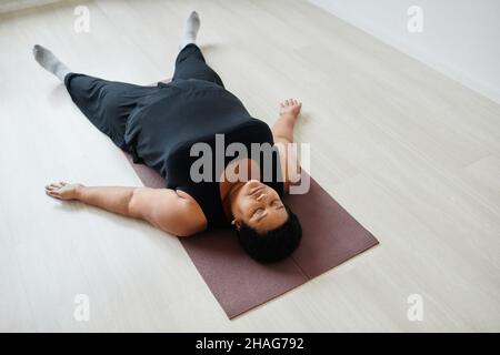 High angle portrait of black senior woman relaxing laying on floor after workout indoors Stock Photo