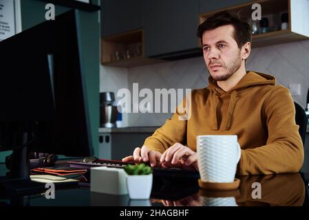 Thirty years old tired man working late remotely at home office, using computer, remote work burnout Stock Photo