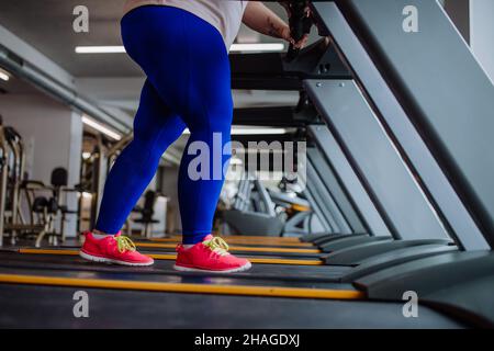 Low section of overweight woman with headphones exercising on treadmill in gym Stock Photo