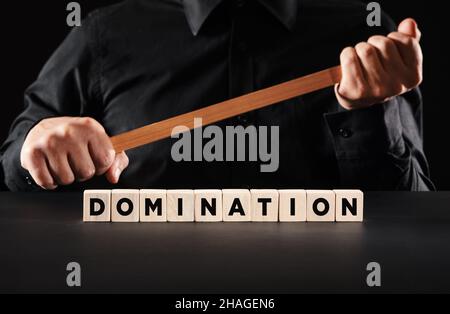 Domination and power concept. Male persons holds a wooden stick with the word domination written on wooden cubes. Stock Photo