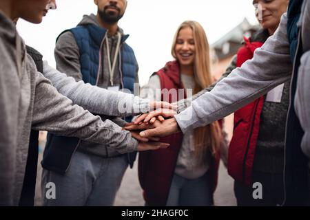 Close up of group of happy community service volunteers stacking hands together outdoors in street Stock Photo
