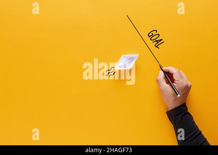 Origami paper boat floats towards a goal line drawn by a male hand. Goal setting or objective achievement in business or education concept. Stock Photo
