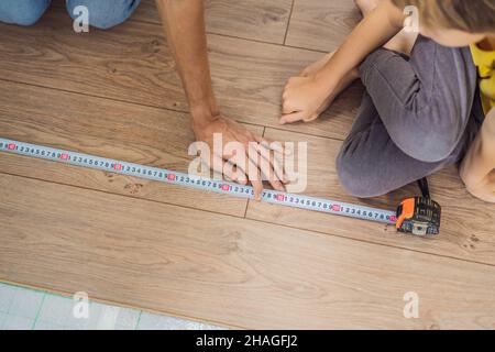 Father and son installing new wooden laminate flooring on a warm film floor. Infrared floor heating system under laminate floor Stock Photo