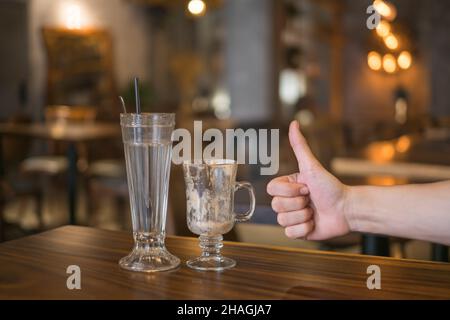 Two empty iced coffee glass cups on the table in coffee shop and hand showing thumbs up sign. High quality photo Stock Photo