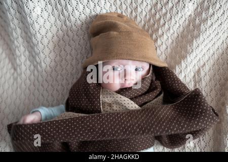 Cute baby with big blue eyes wearing a hat and a huge knitted scarf Stock Photo