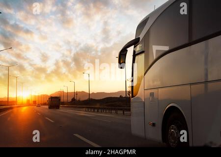 A bus is traveling on the asphalt highway roadrural land against the sunset. Travel and transport concept. High quality photo Stock Photo