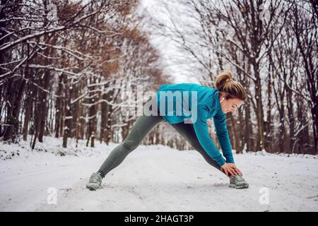 Fit sportswoman standing in snow in forest and doing fitness exercises. Healthy life, winter fitness Stock Photo