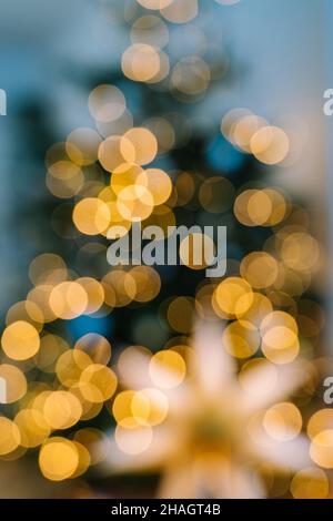 Christmas tree in interior with defocused lights and star. Christmas abstract blur background. Out of focus holiday background with christmas tree. Light bokeh from Xmas tree. Xmas and New Year theme. Stock Photo