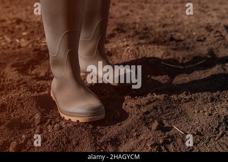 Close up of female farmer in rubber boots standing in the ploughed field, selective focus Stock Photo