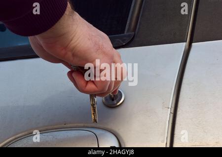 A man's hand inserts a key into the keyhole of a used car door. There are several keys in hand. Stock Photo
