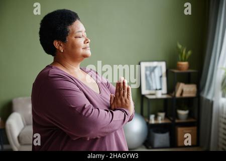 Side view waist up portrait of black senior woman meditating at home with eyes closed Stock Photo