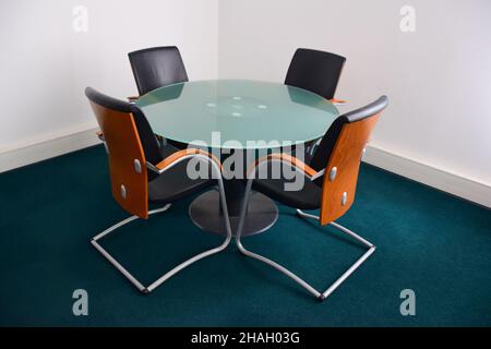 Four empty leather decorative office chairs with wooden backs sit around a glass circular table. Side view Stock Photo