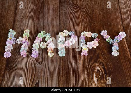 On a dark wooden background, the word HAPPY is lined with multicolored flowers in large letters. Stock Photo