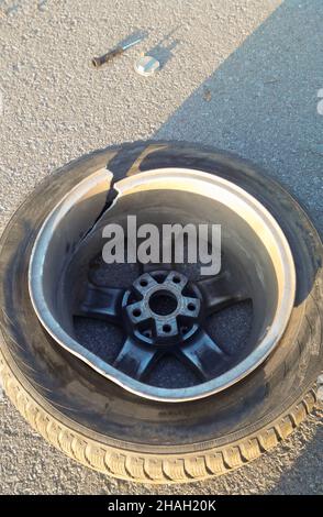 On the asphalt close-up lies a wheel from a car with a split alloy wheel, smashed in a hole on the road Stock Photo