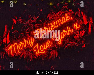 An illuminated red neon sign with a background of green foliage offers Christmas greetings to visitors of the Christmas Markets in the City of York. Stock Photo
