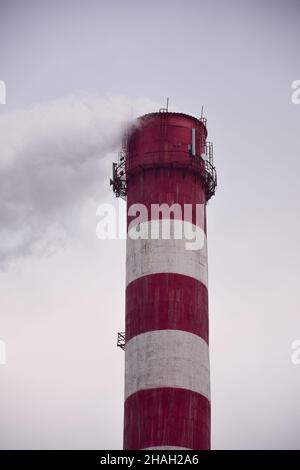 Steaming striped chimney of a plant or factory on a sky background Stock Photo